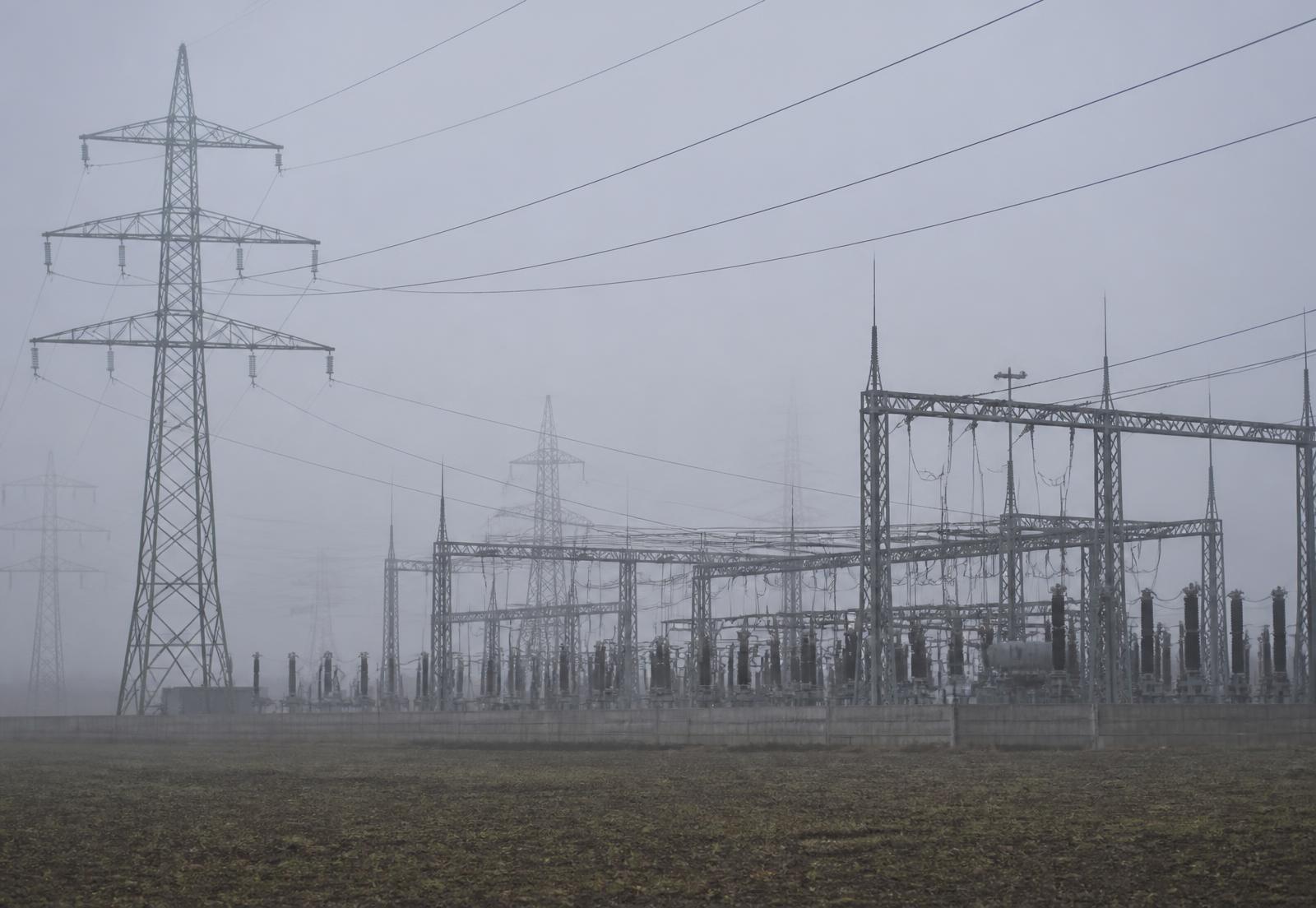 Umspannanlage und Hochspannungsmasten in einer nebligen, offenen Landschaft