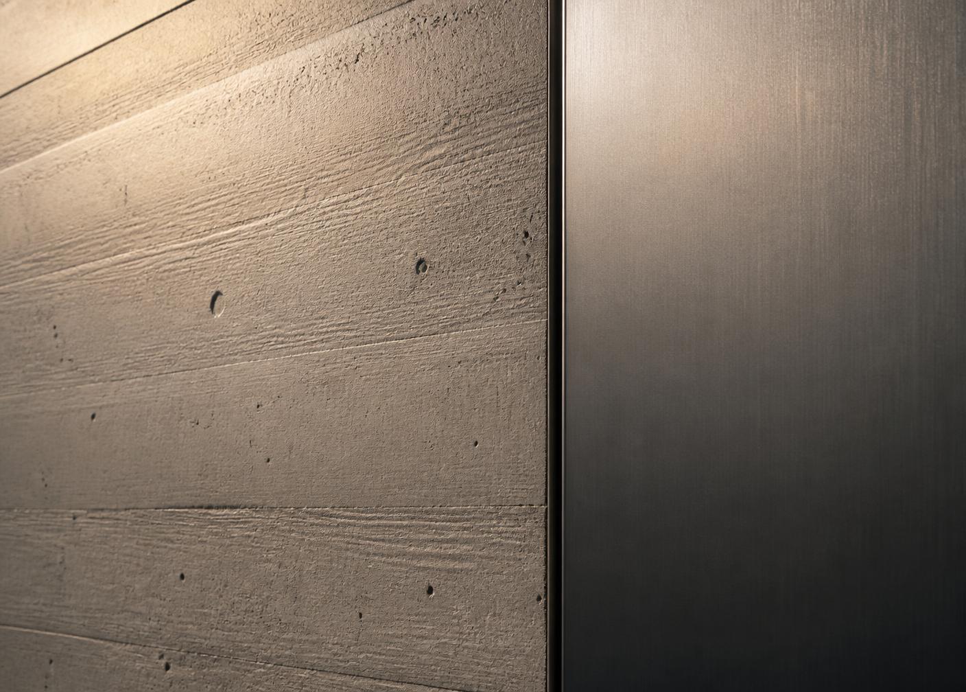 Detail einer brettgeschalten Betonwand neben einer dunkel gebürsteten Stahlfläche